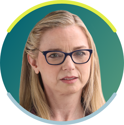 A white woman with long blonde hair and dark glasses faces the camera with a neutral smile.