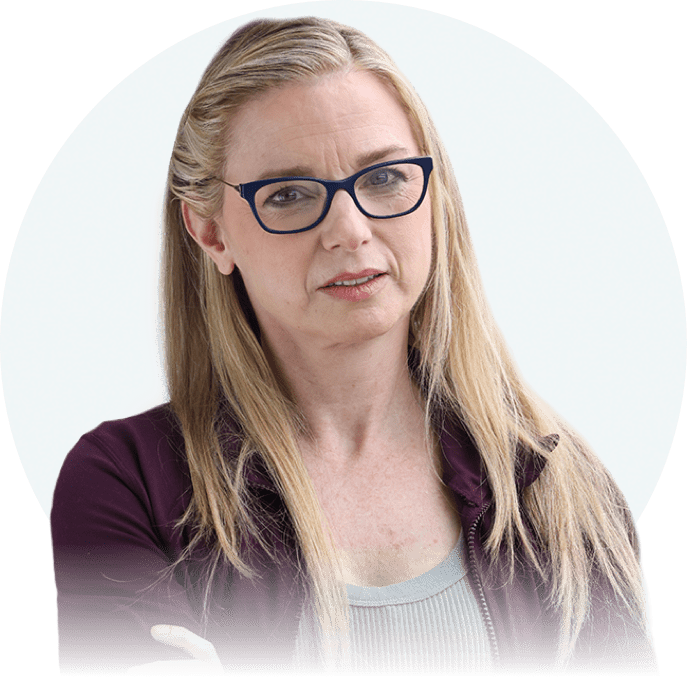 A white woman with long blonde hair and dark glasses is seen from the chest up. She is facing the camera with a concerned expression