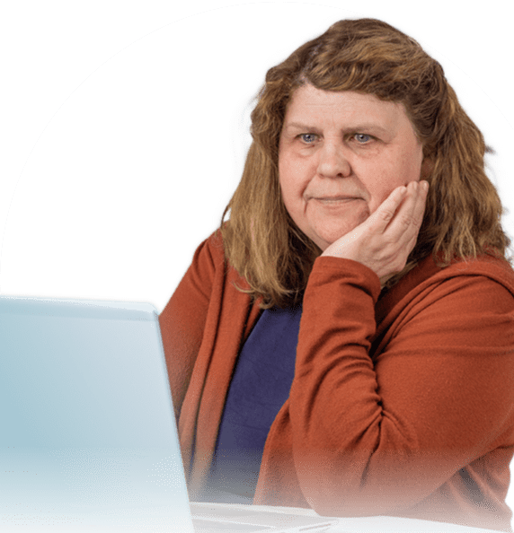 A white woman with brown hair is seen from the waist up. She is seated and looking at a laptop